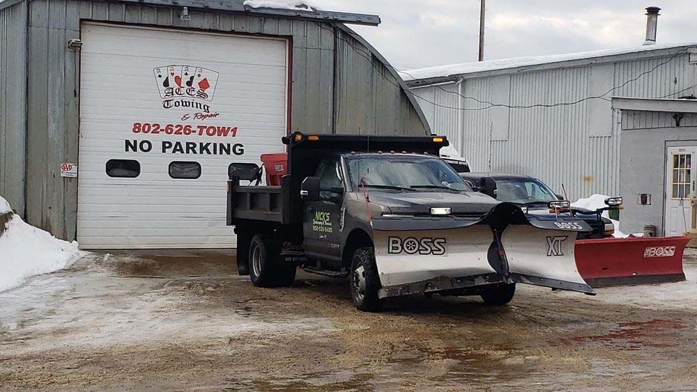 A snow plow is parked in front of a building that says no parking