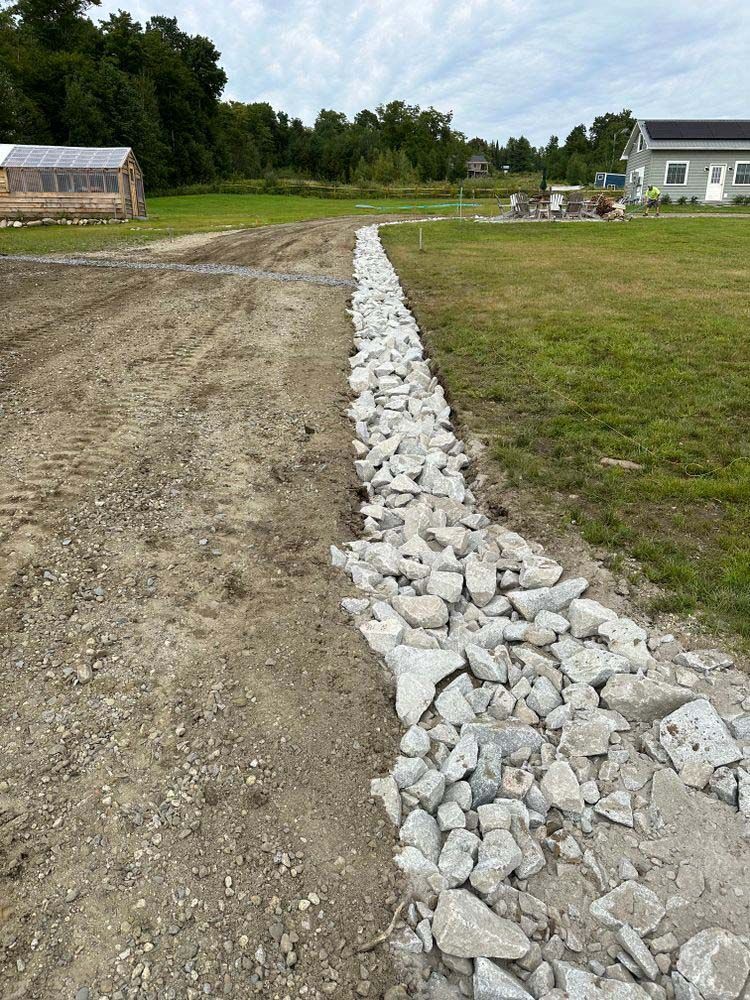 A pile of rocks is sitting on the side of a dirt road next to a grassy field.