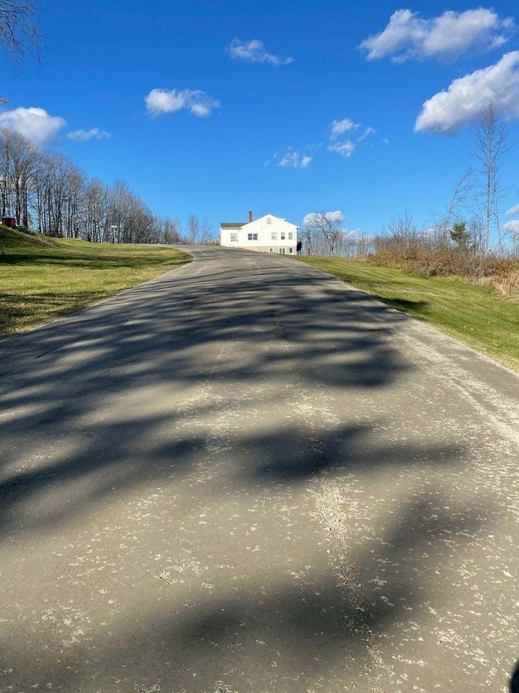 A dirt road with a white house on the side of it