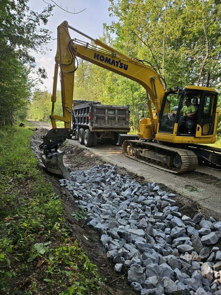 A yellow excavator is driving down a road next to a dump truck.