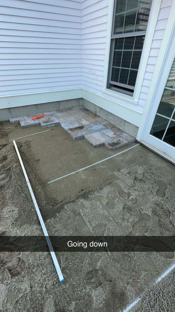 A person is laying tiles on a patio in front of a house.