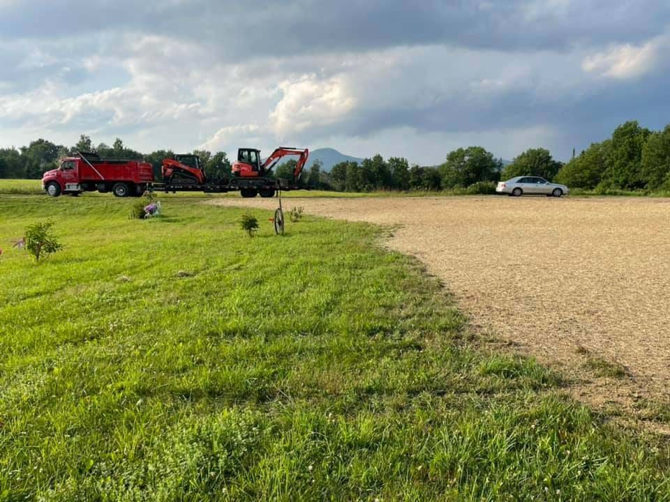 A red dump truck is parked in a grassy field next to a gravel road.