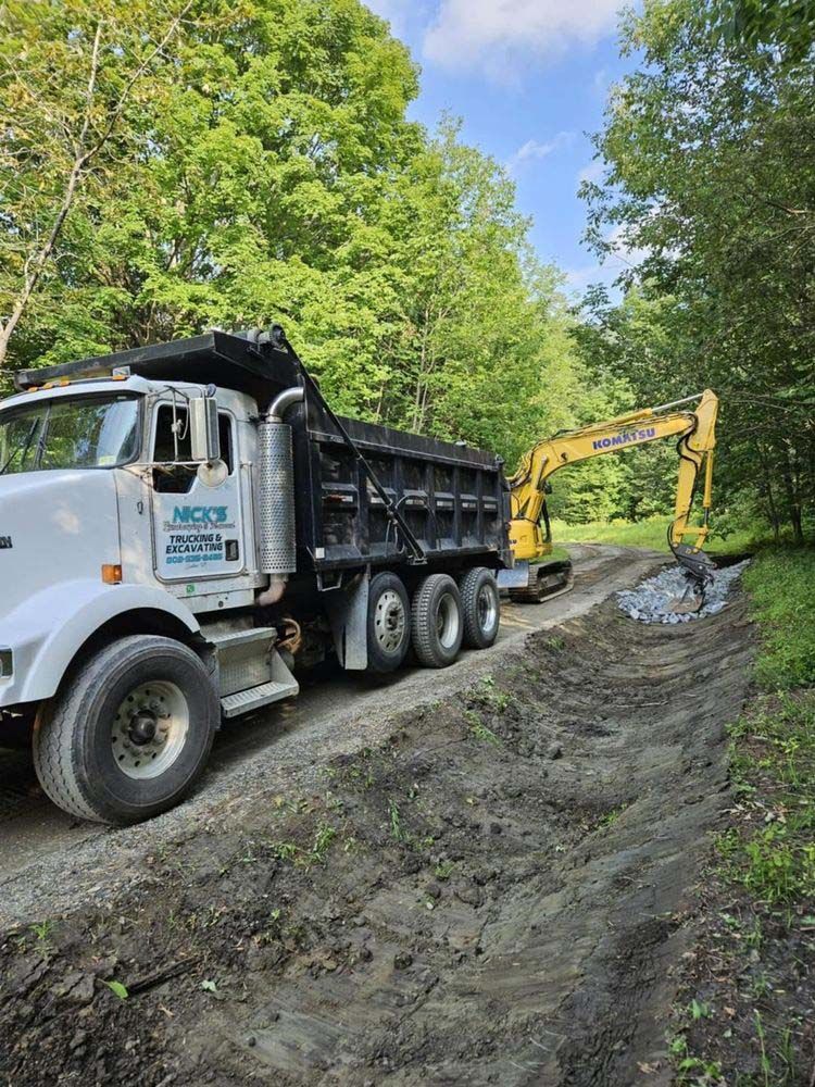 A dump truck is driving down a dirt road next to an excavator.