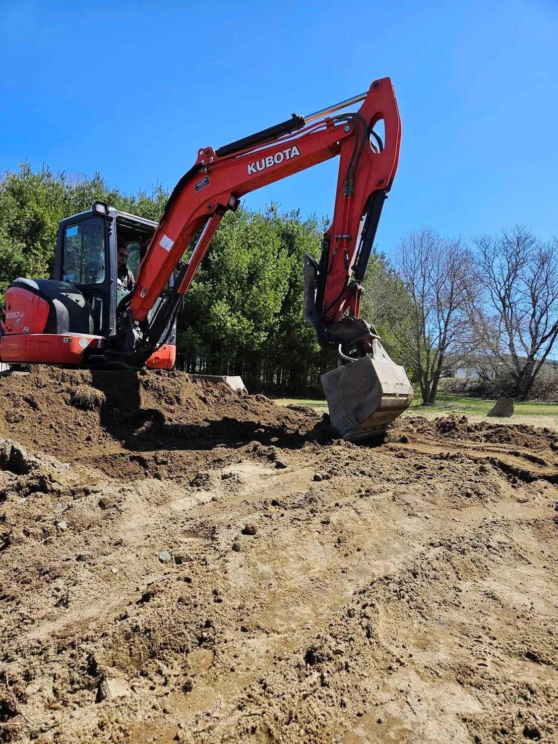 A red excavator is digging a hole in the dirt.