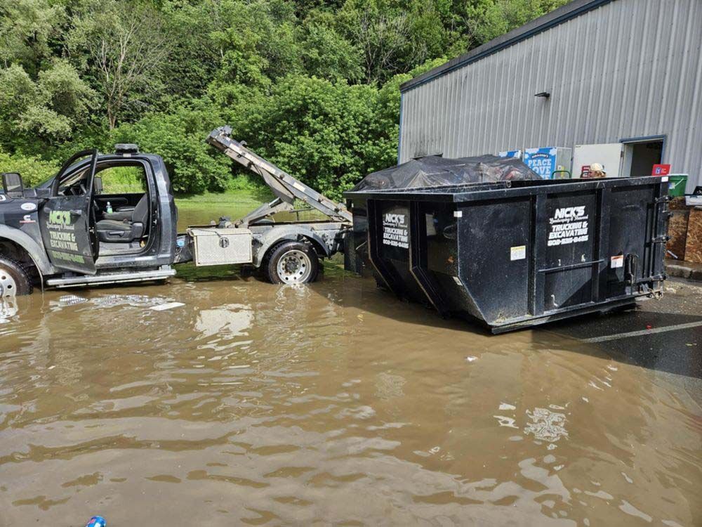 A truck is towing a dumpster through a flooded area.