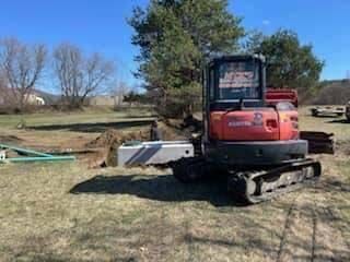 A red excavator is parked in a grassy field.