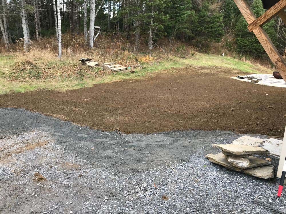 A gravel driveway leading to a lush green field with trees in the background.