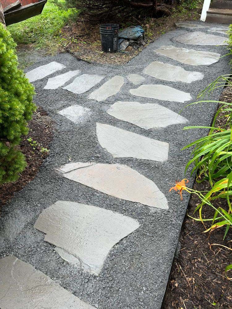 A stone walkway in a garden with a bucket in the background.