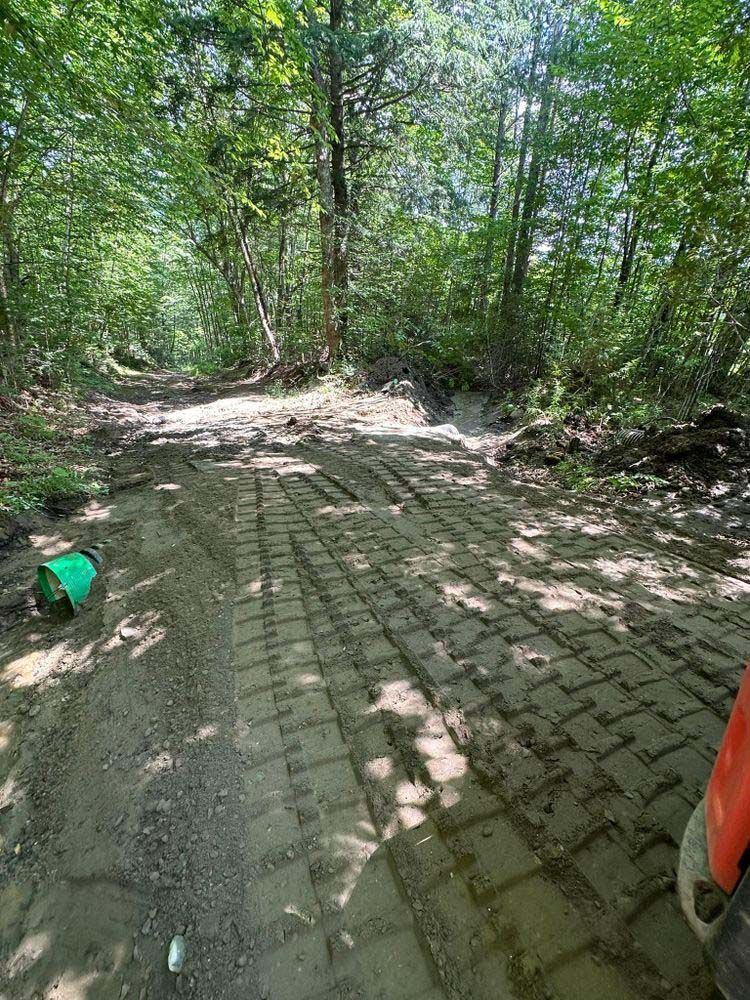 A tractor is driving down a dirt road in the woods.