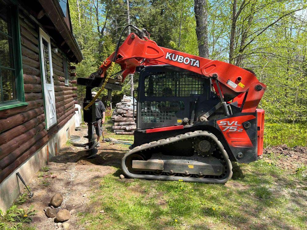 A red and black kubota skid steer is parked in front of a wooden house.