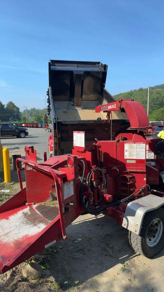A red wood chipper is parked next to a dump truck in a parking lot.