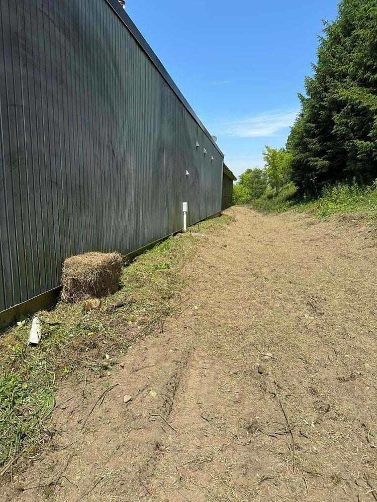 A dirt road leading to a building with a bale of hay on the side of it.