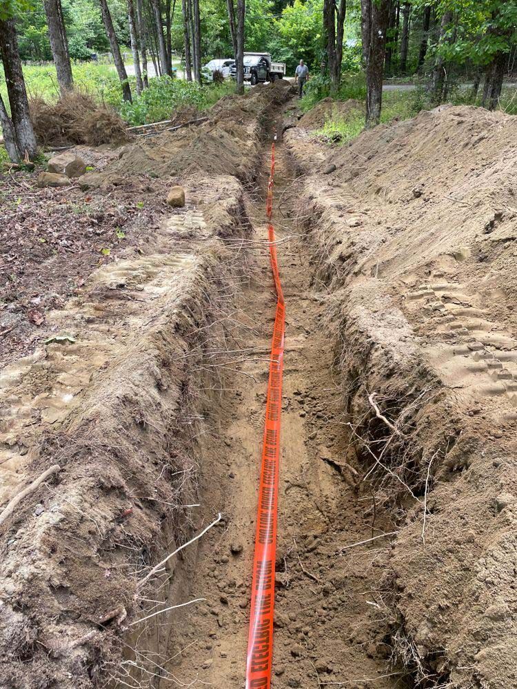 An orange pipe is being installed in a trench in the dirt.