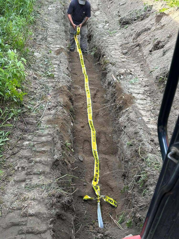 A man is kneeling in the dirt holding a yellow tape measure.