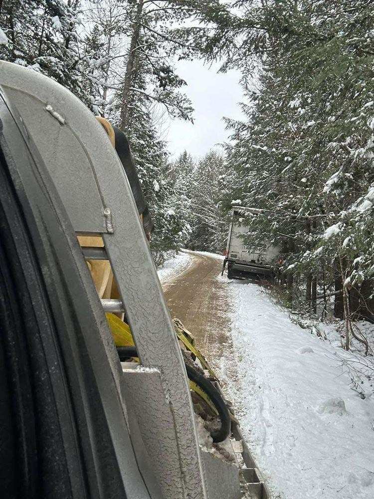 A truck is driving down a snowy road in the woods.