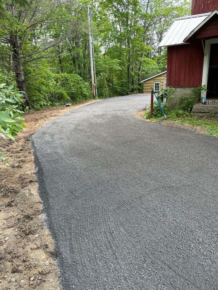 A dirt road leading to a red barn in the woods.