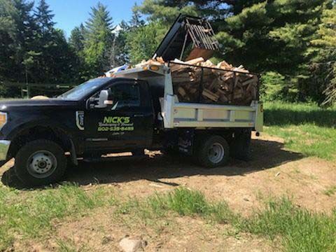 A dump truck filled with wood is parked in a field.