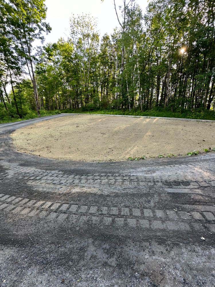 A dirt field in the middle of a forest with trees in the background.