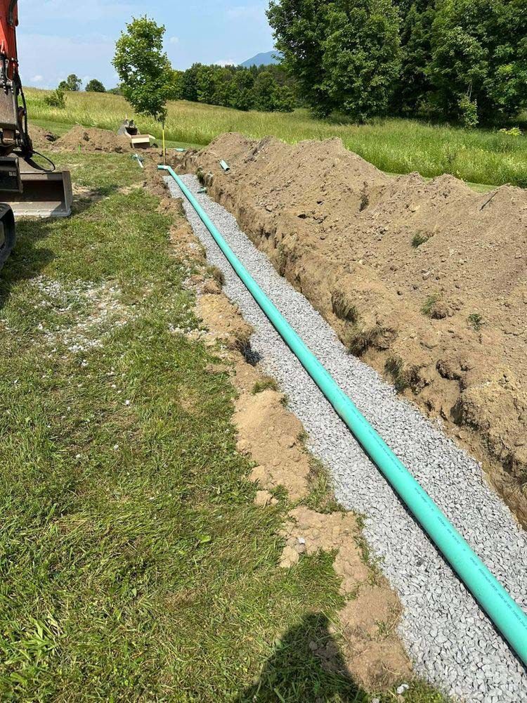 A green pipe is being installed in a trench in a field.