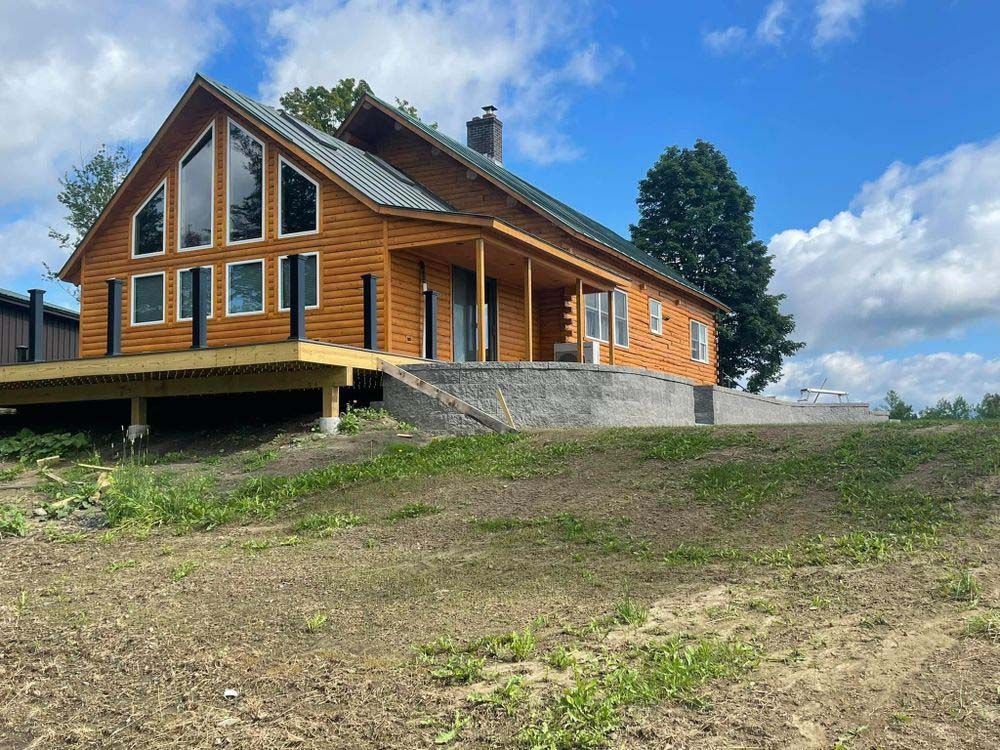 A large log cabin is sitting on top of a grassy hill.