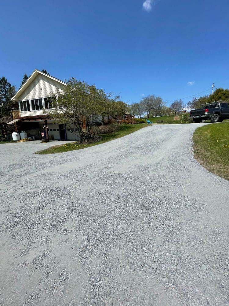 A gravel driveway leading to a house with a truck parked on the side of it.