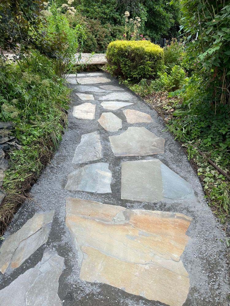 A stone walkway in a garden surrounded by trees and bushes.