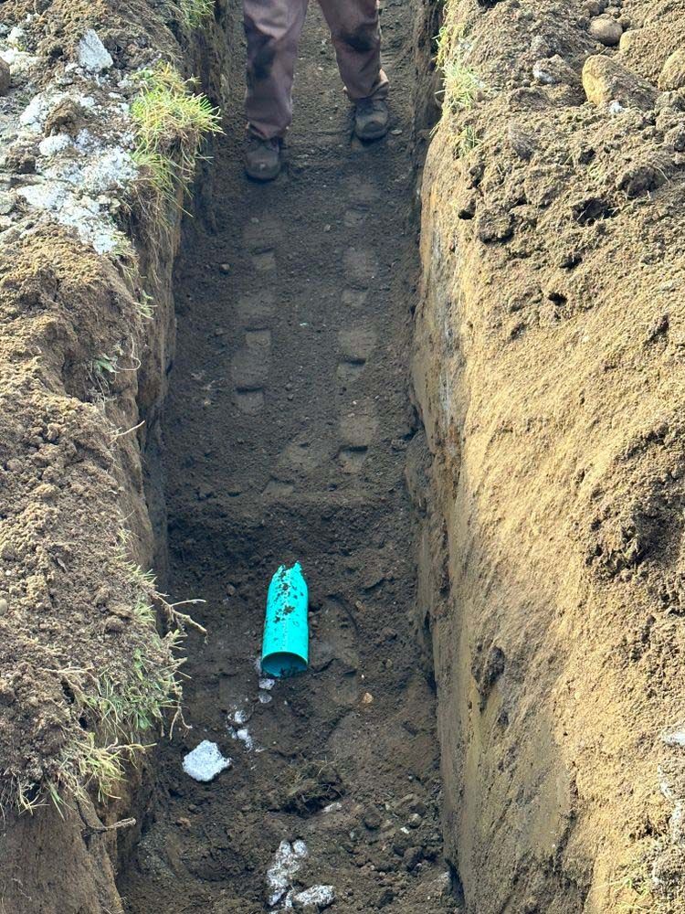 A man is standing in a trench next to a blue pipe.