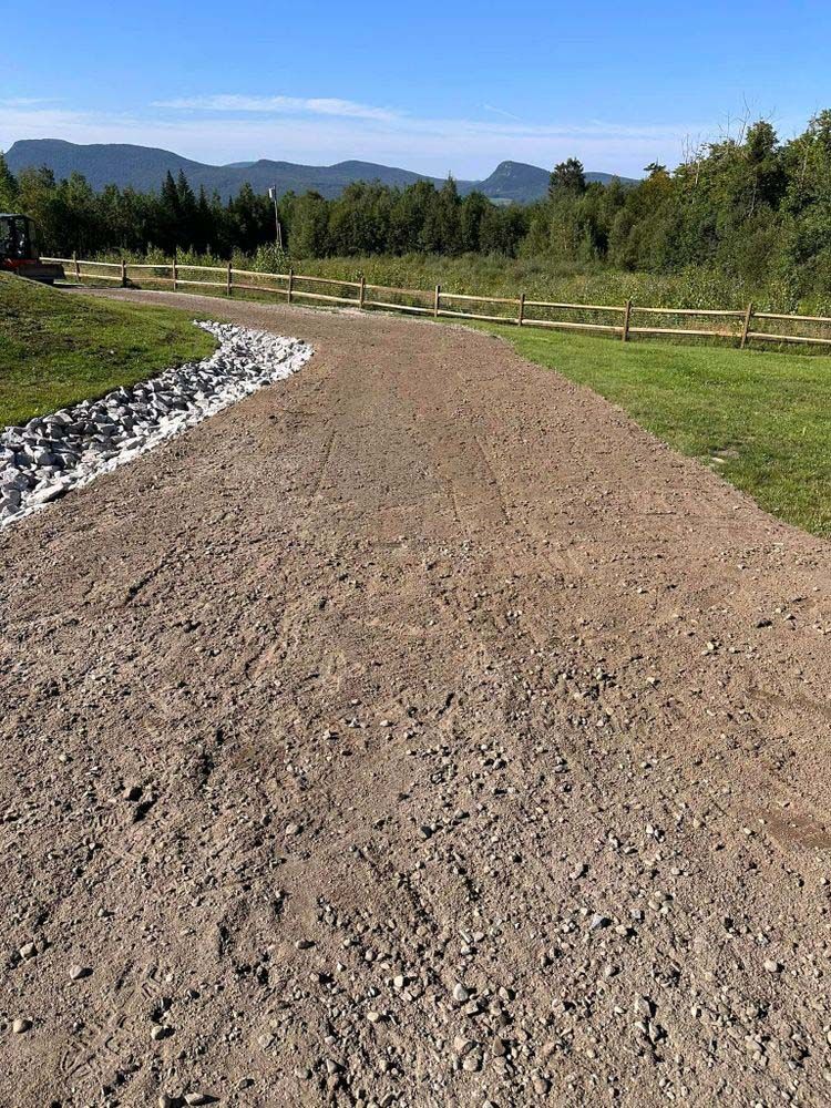 A dirt road going through a grassy field with a fence in the background.
