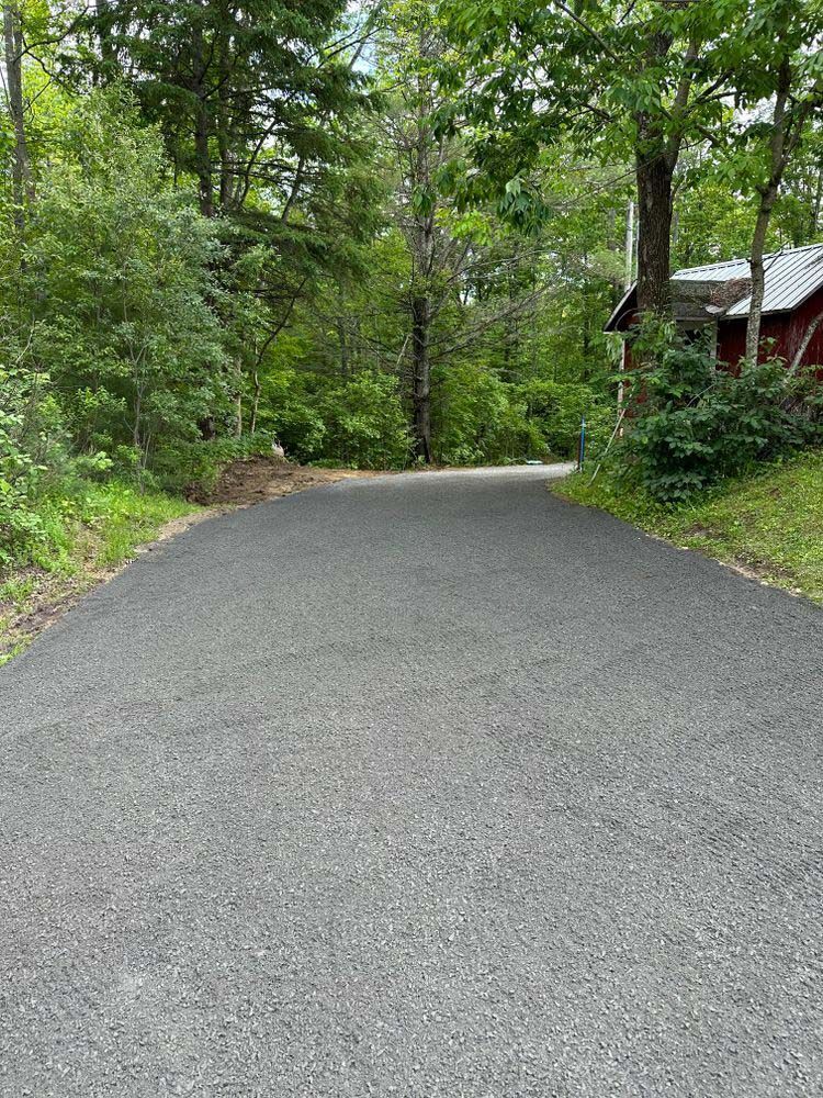 A road going through a forest with trees on both sides and a red house in the background.