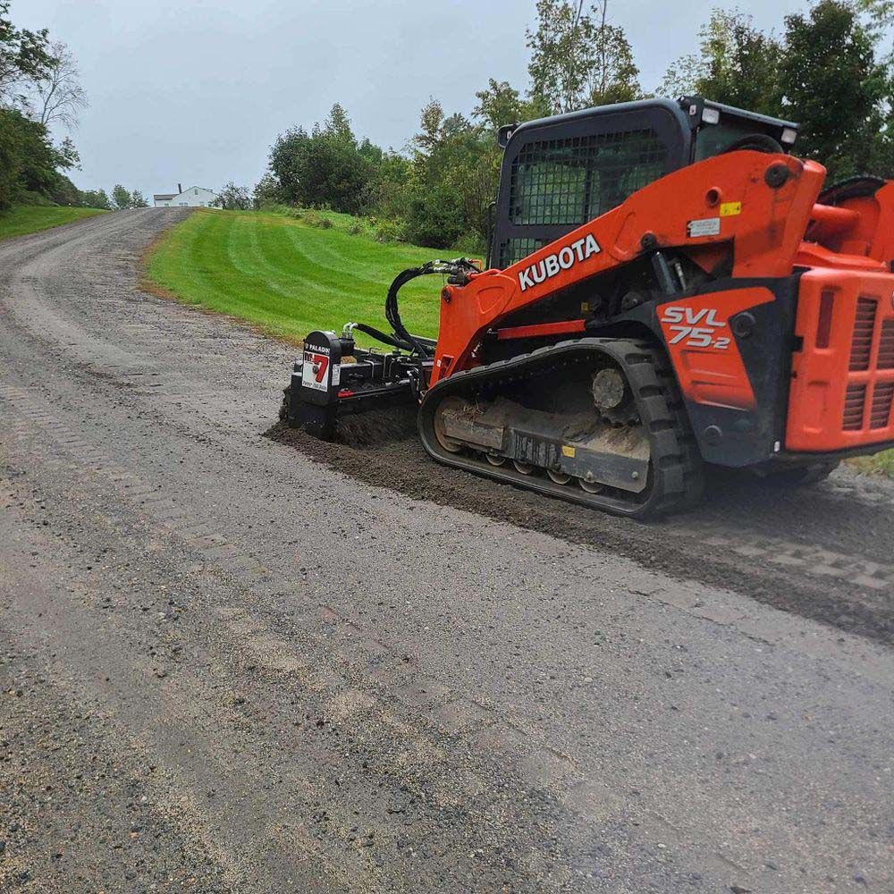 A kubota skid steer is driving down a dirt road.
