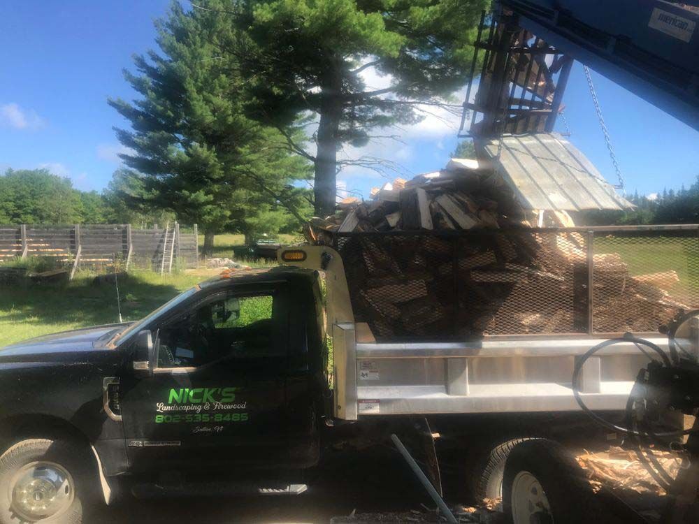A dump truck is being loaded with logs by a crane.