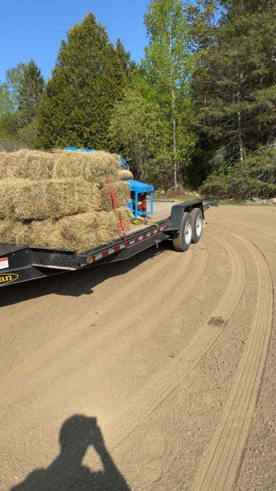 A trailer filled with hay bales is driving down a dirt road.