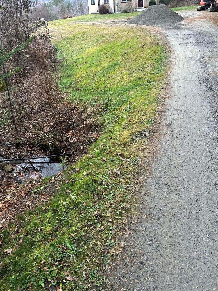A dirt road going through a grassy field next to a house.