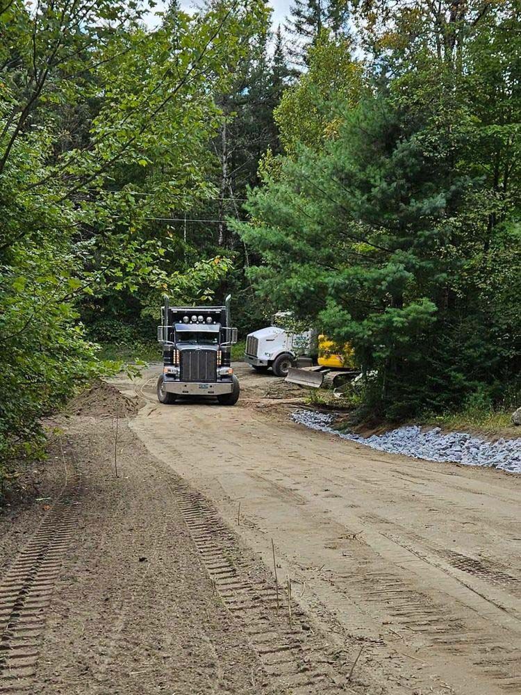 A truck is driving down a dirt road in the woods.