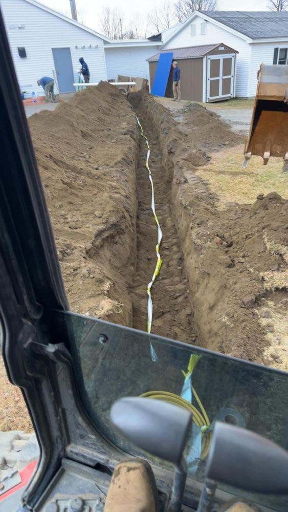 A construction vehicle is digging a trench in the dirt in front of a house.
