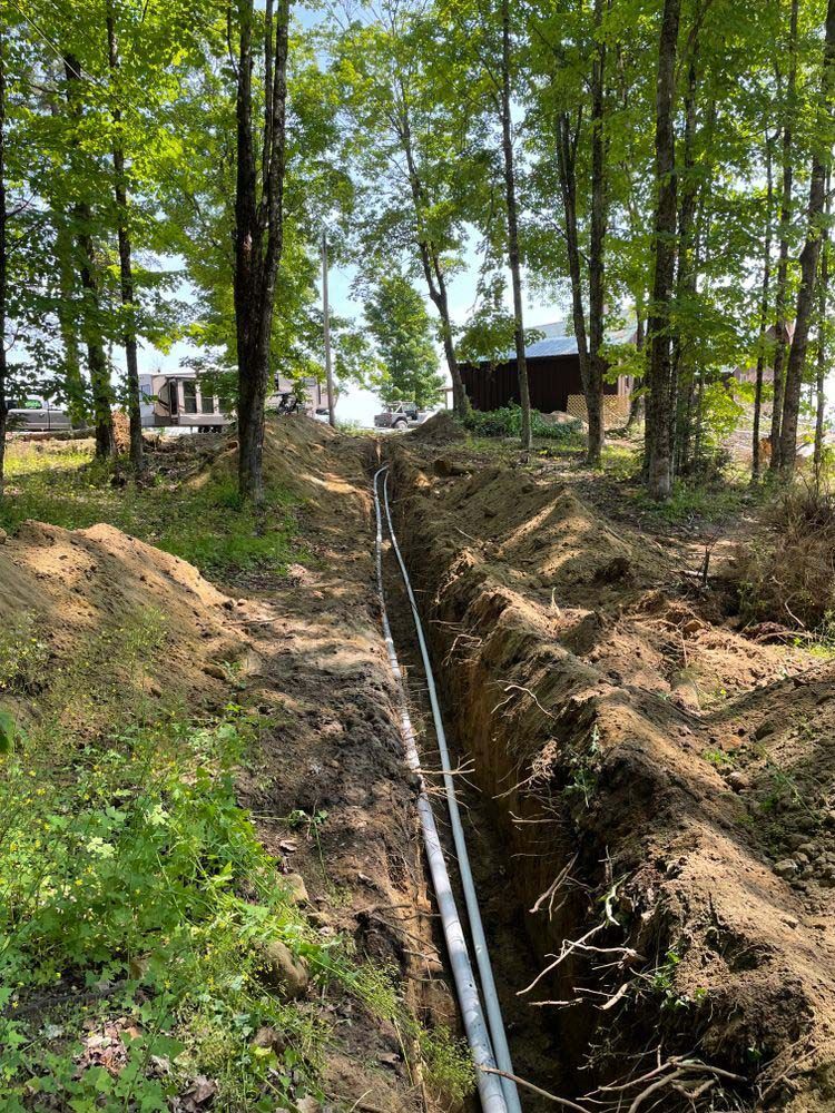 A pipe is being installed in a trench in the woods.