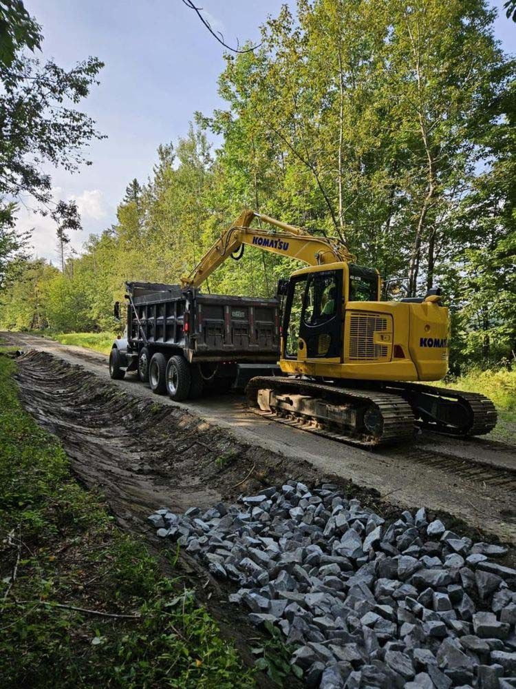 A yellow excavator is loading a dump truck on a dirt road.