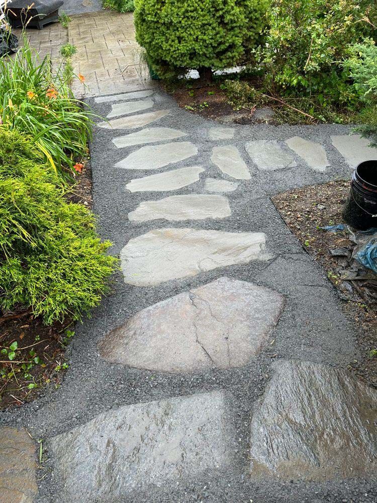 A stone walkway in a garden surrounded by trees and bushes.