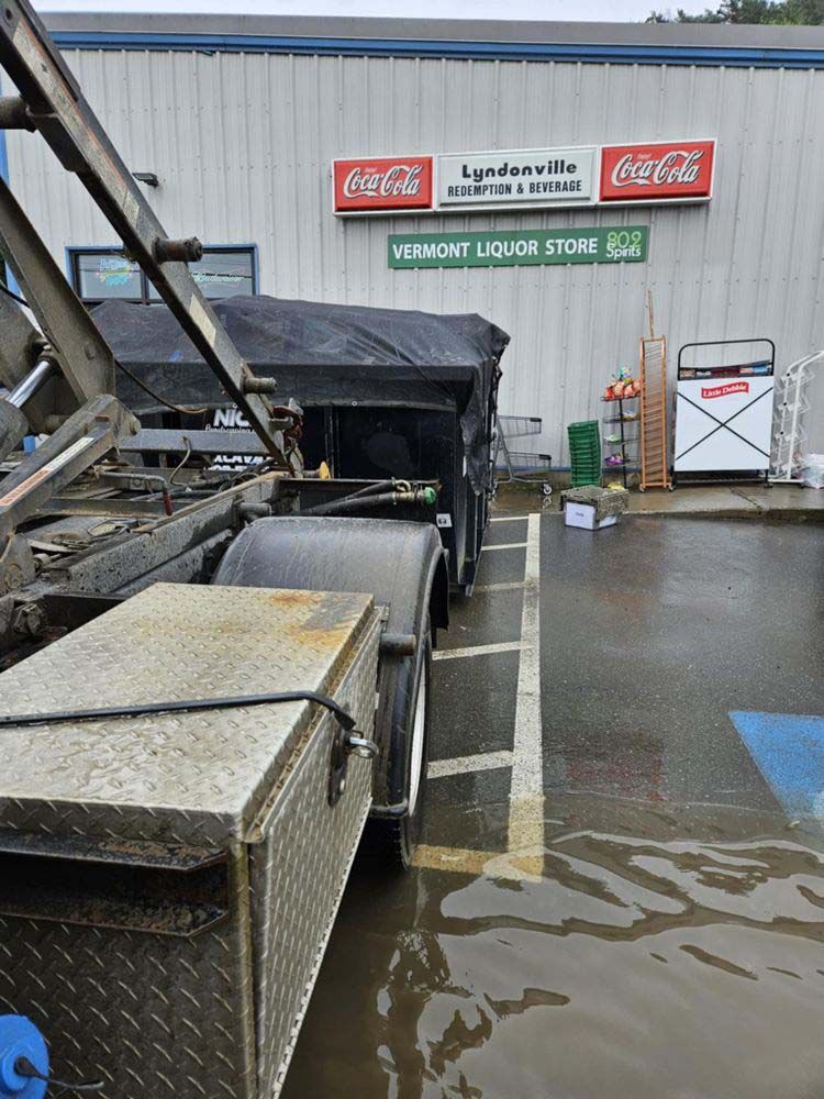 A truck is parked in a flooded parking lot in front of a liquor store.