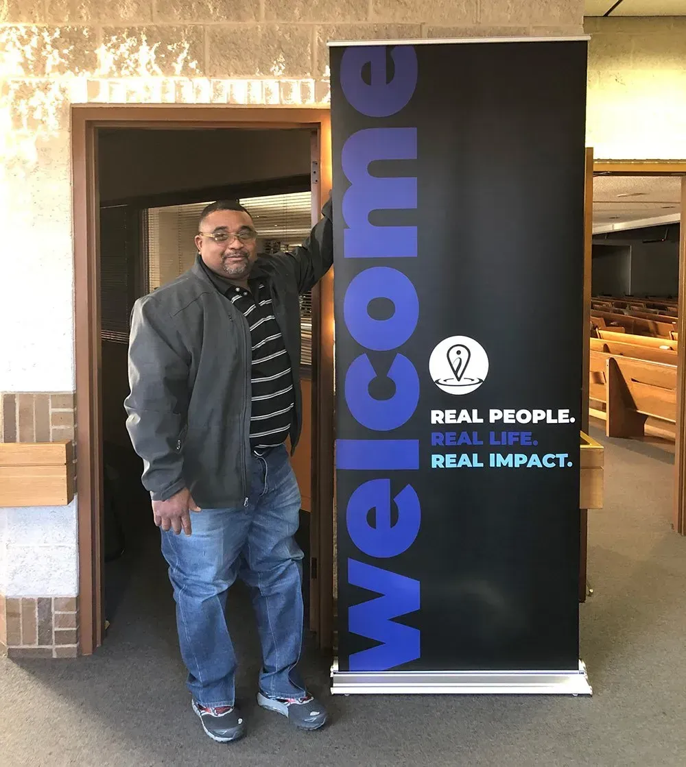 A man stands in front of a welcome sign A man stands in front of a welcome sign
