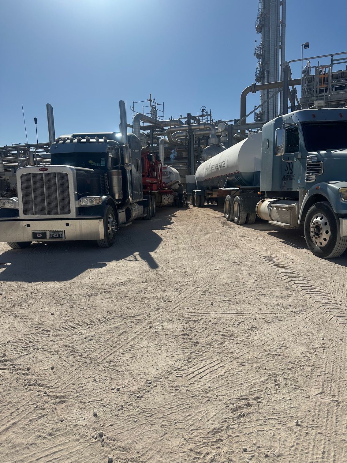Two semi trucks are parked next to each other on a dirt road.