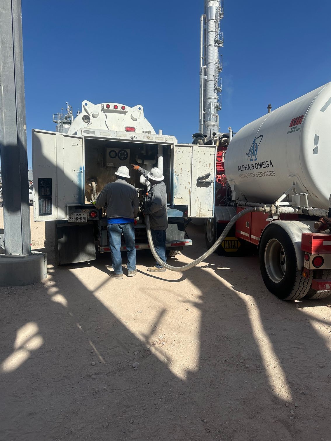 Two men are standing in front of a tanker truck.