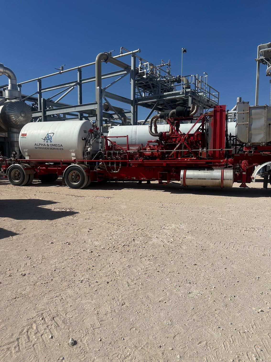 A truck with a tanker on the back is parked in front of a factory.
