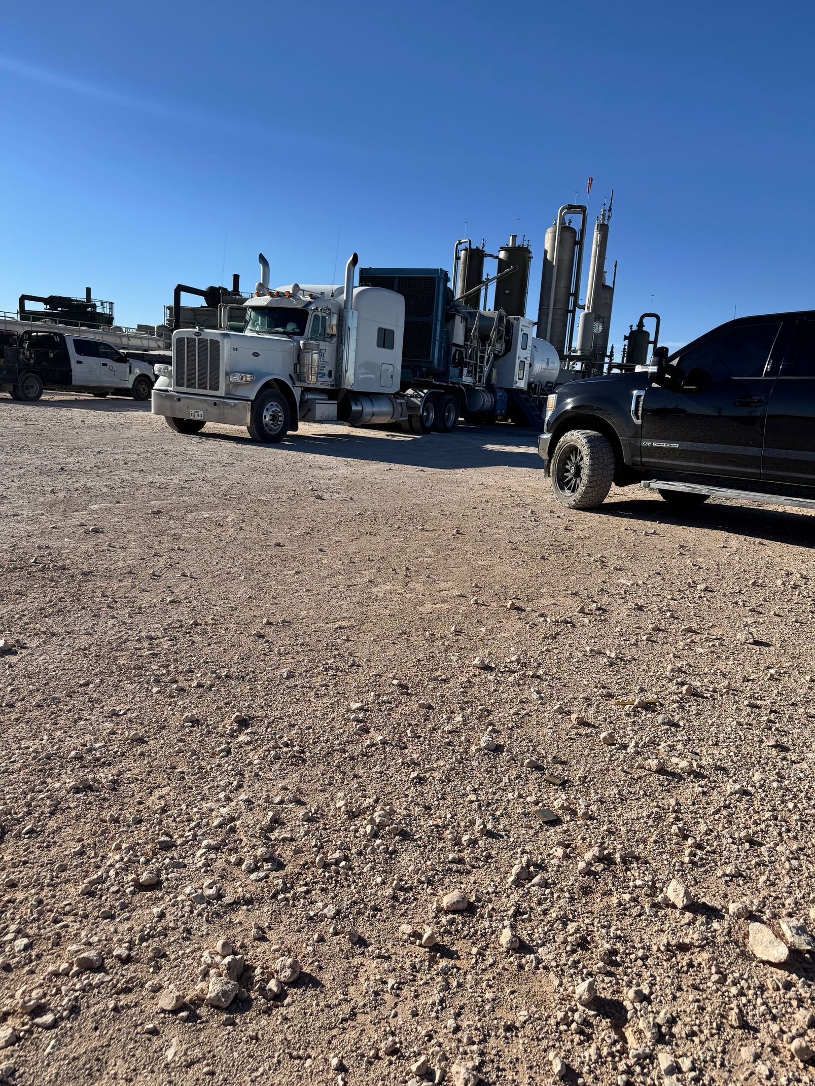A truck and a car are parked in a gravel lot.