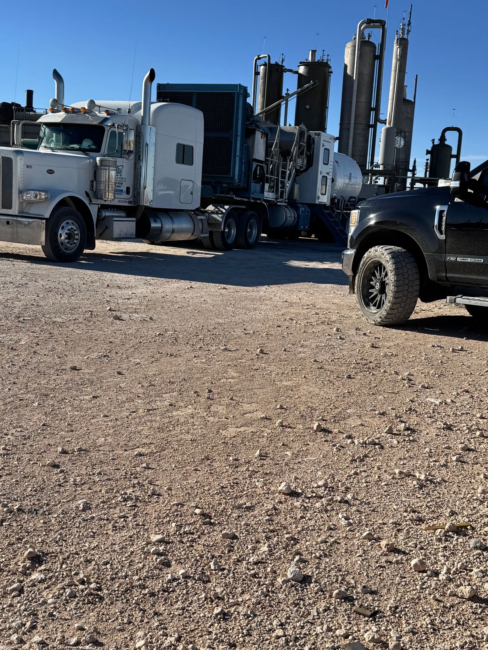 Two semi trucks are parked next to each other in a gravel lot.
