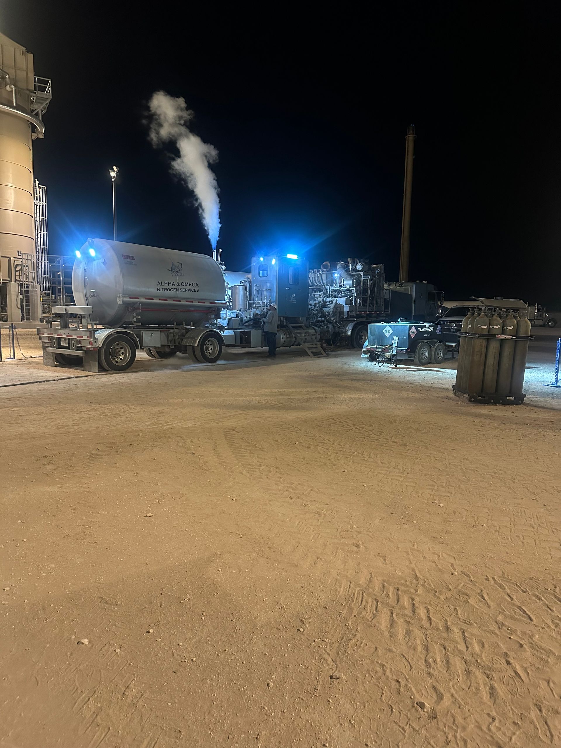 A large tanker truck is parked in a parking lot at night.