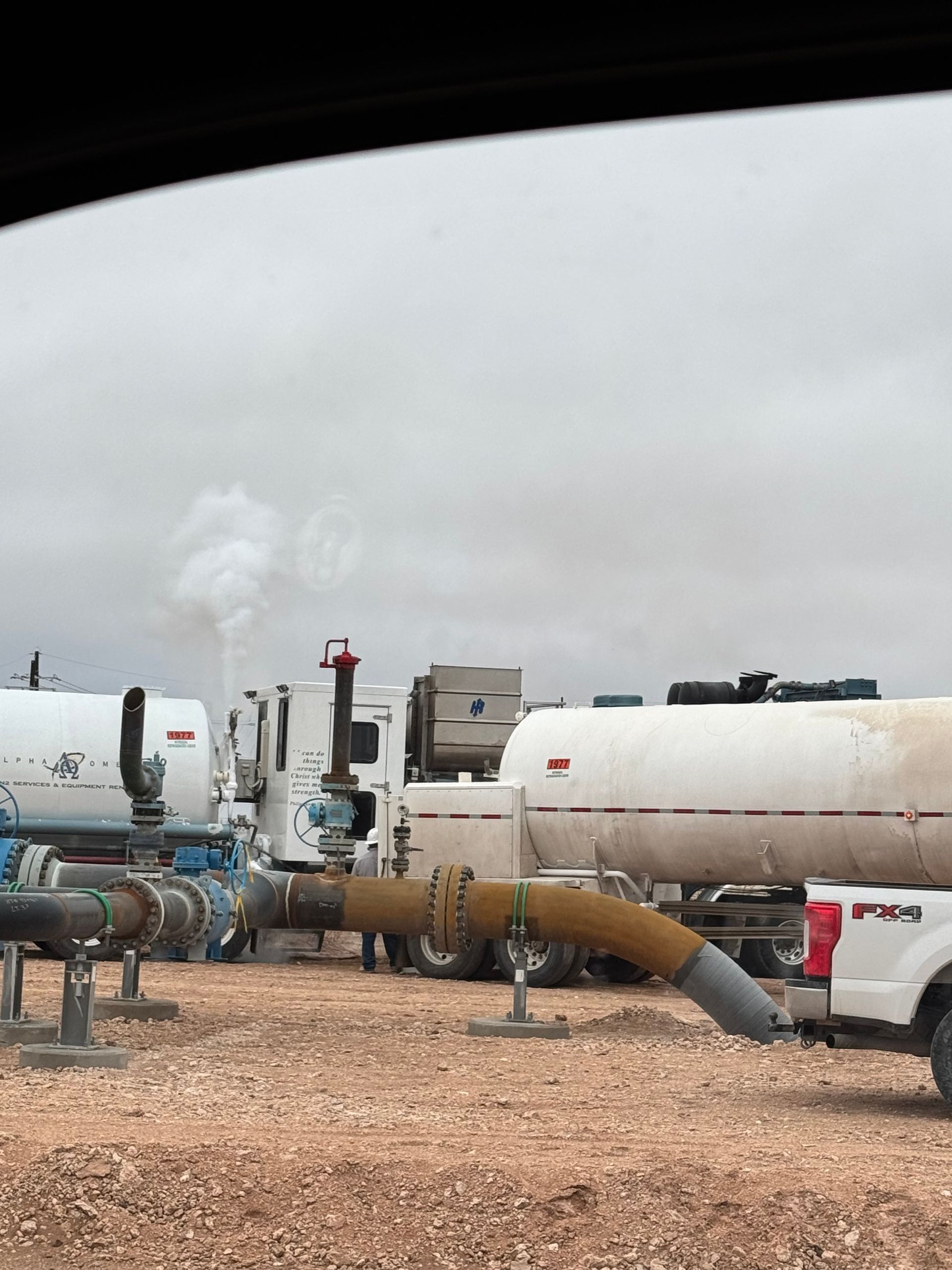 A row of trucks are parked in a field with pipes coming out of them.