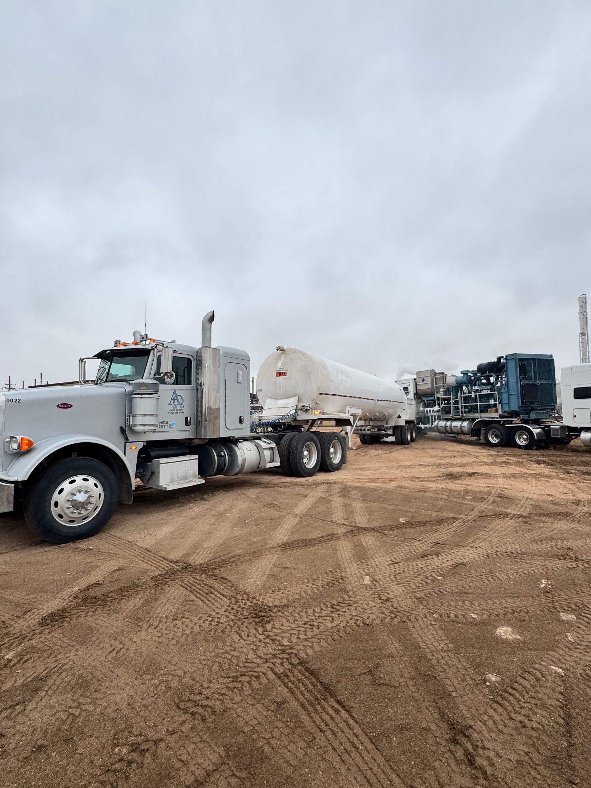 A row of semi trucks are parked in a dirt field.