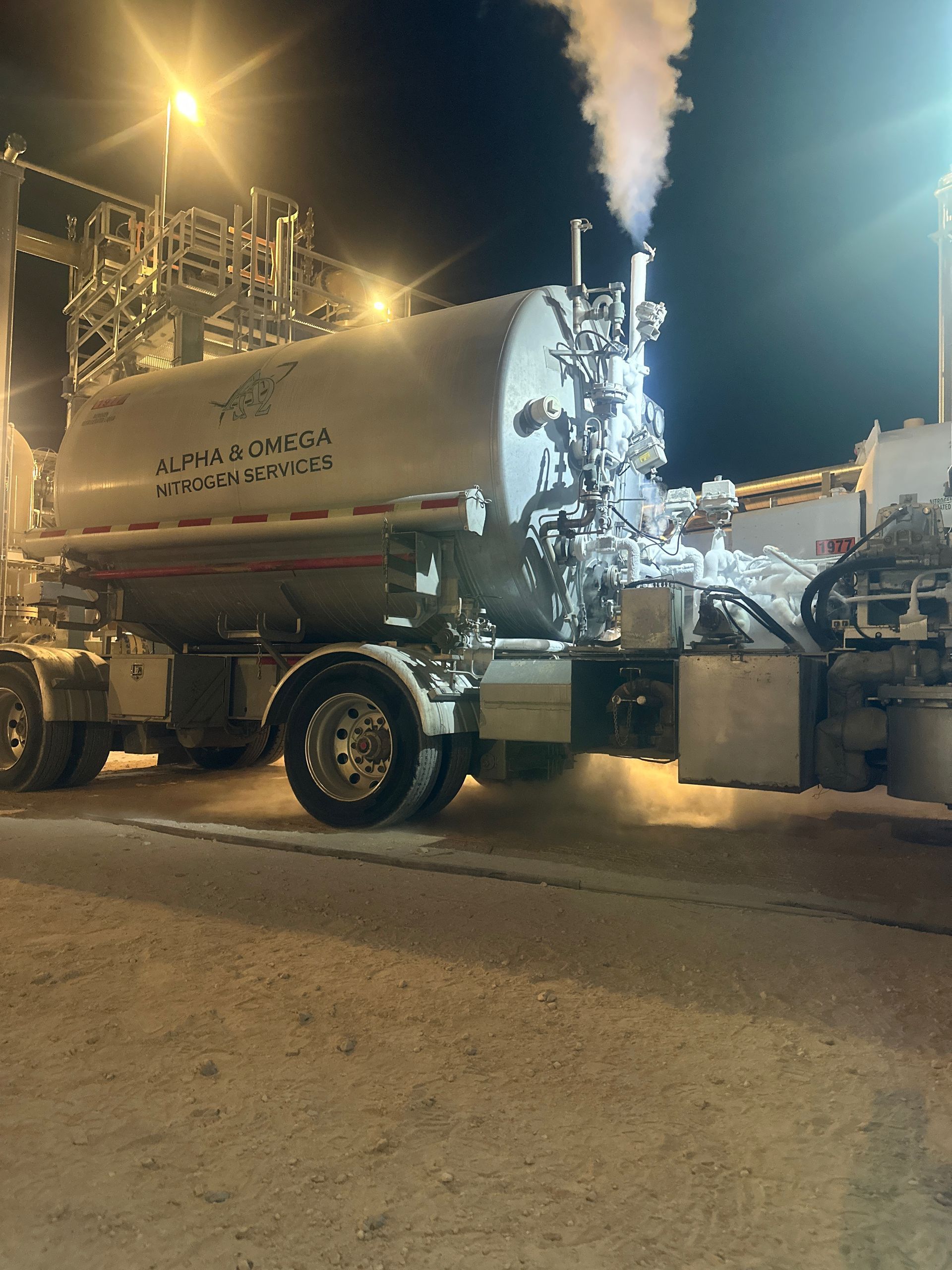A large tanker truck is parked on the side of the road at night.