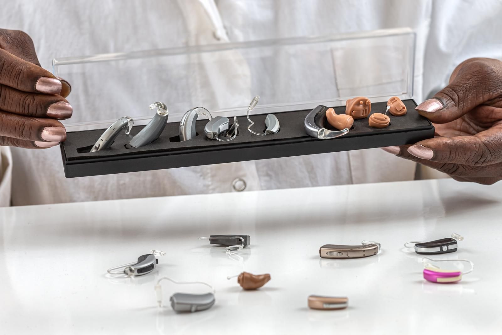 Person holding a tray displaying various hearing aids of different sizes and styles.